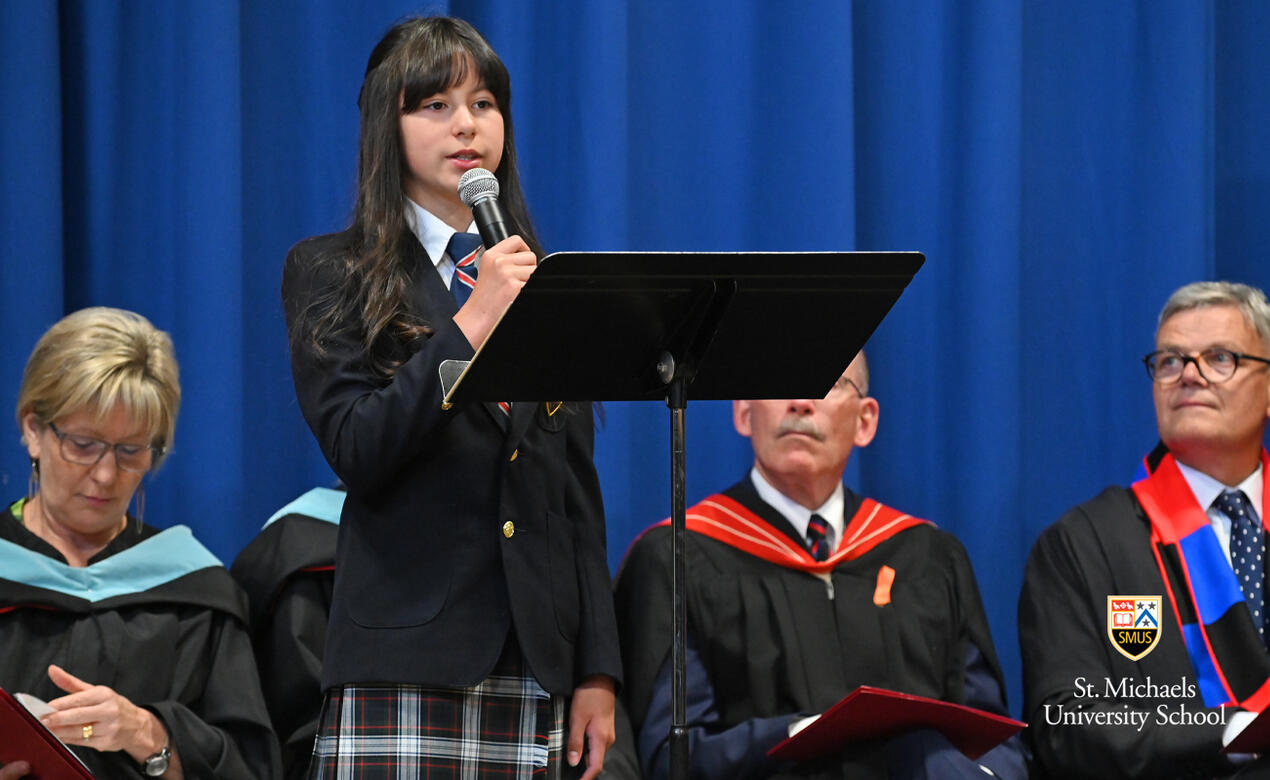 Grade 5 student Abi speaks on stage during the Closing Ceremony, while administrators look on.