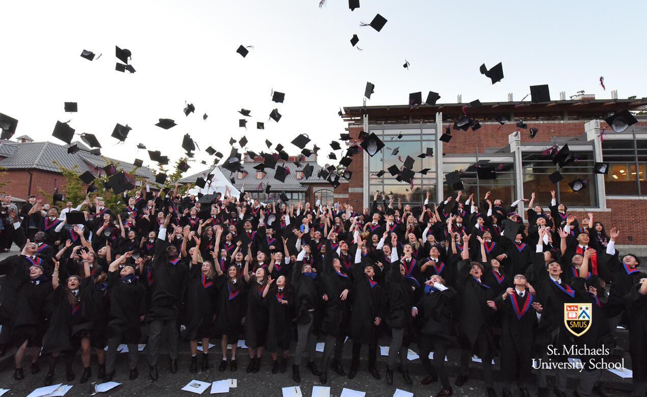 A large group of Grade 12 students toss their caps in the air after graduation
