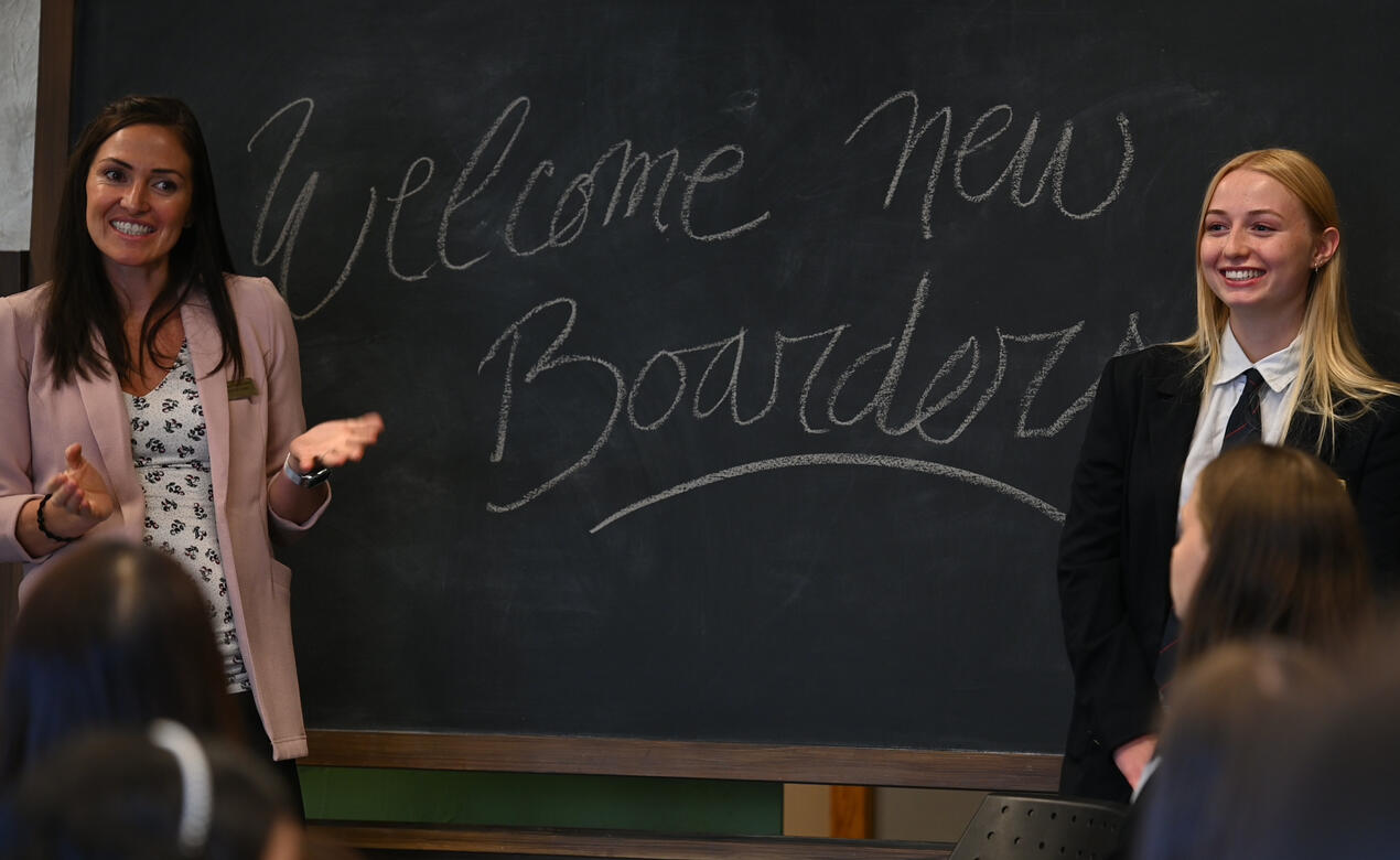 Two speakers stand in front of a sign that reads Welcome New Boarders