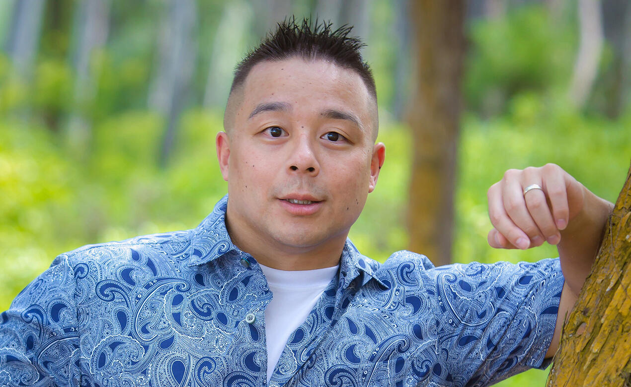 A man poses against a tree