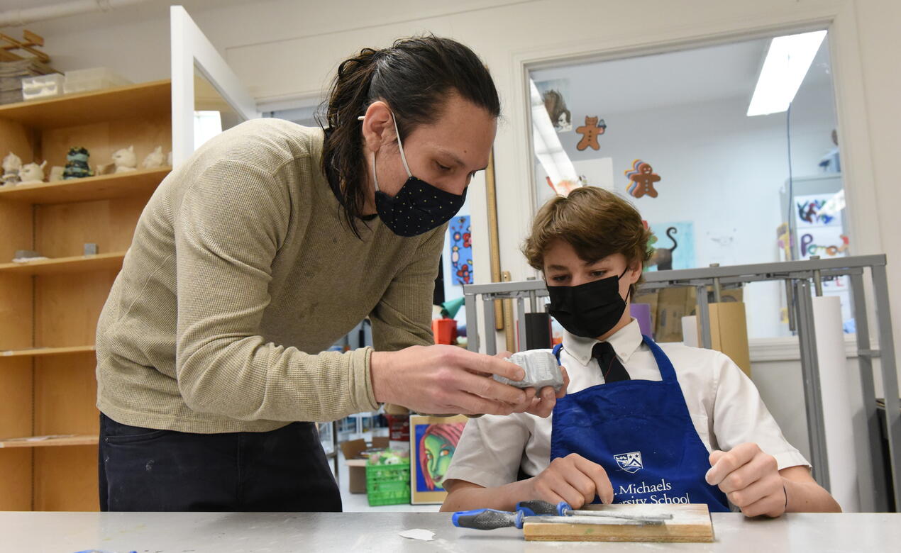 Artist Dylan Thomas works with a Middle School student to demonstrate soapstone carving in an art classroom.