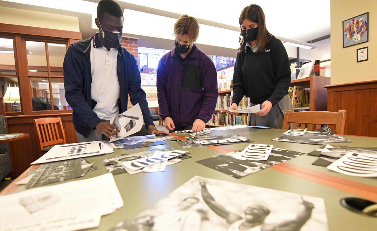 A group of students work at a table with a variety of paper cut out to create a timeline.