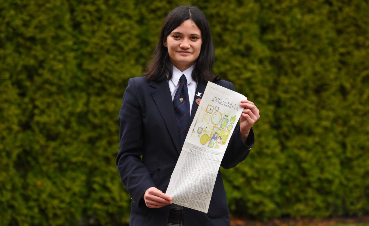 A Senior School student holds up a newspaper clipping.