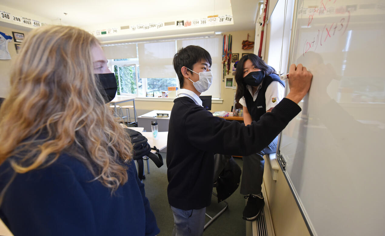 Senior School students stand together working on a math problem on a whiteboard.