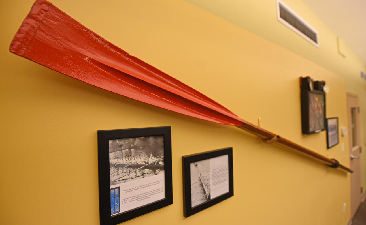 A red-bladed rowing oar is mounted on a wall.