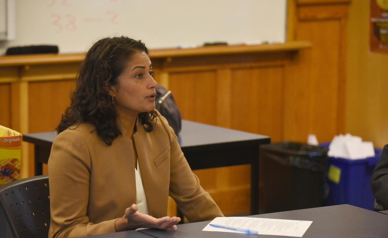 Alumna Gargee Ghosh '93 sits at a table in a classroom in conversation.