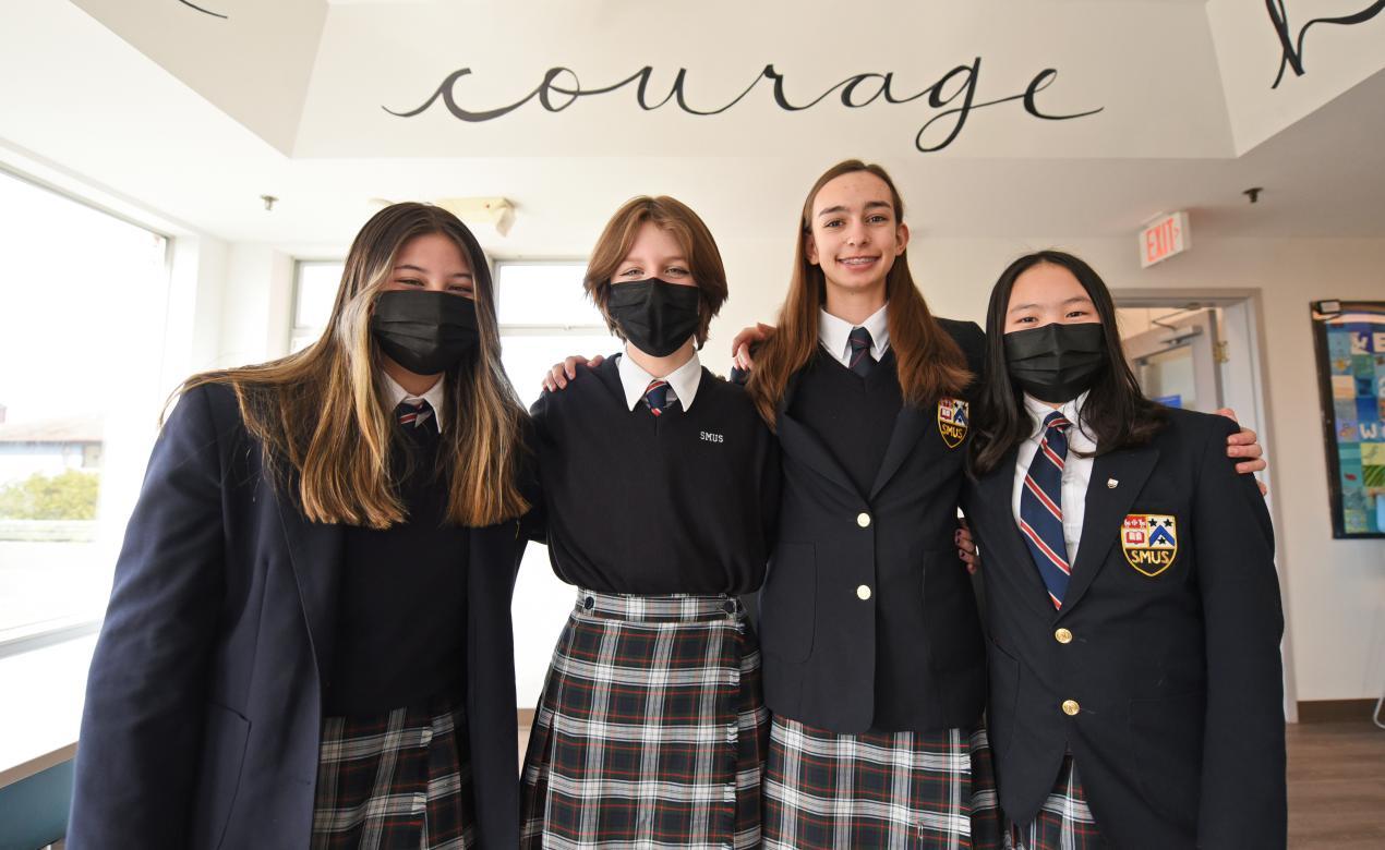 Four Grade 8 students pose together in front of a sign that reads Courage