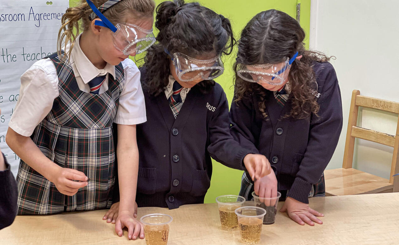 Three young students watch a science experiment involving raisins and pop