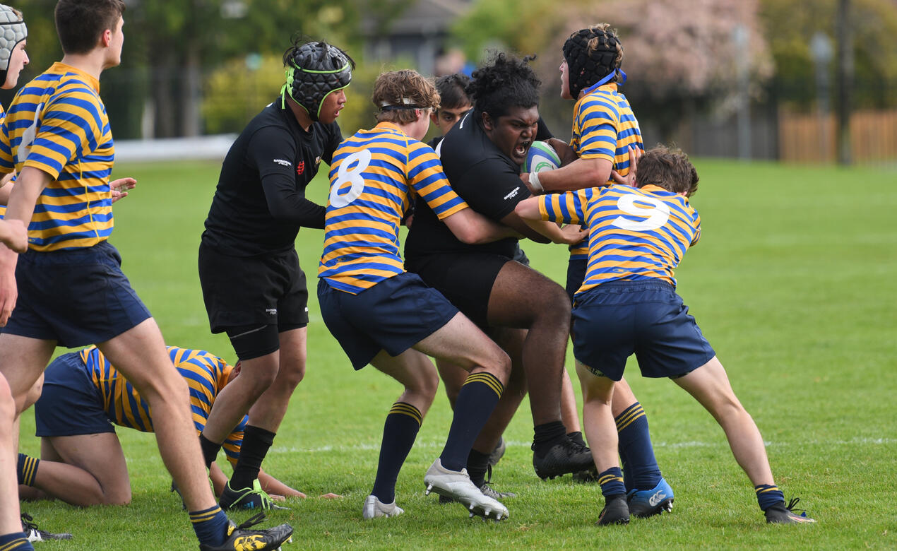 A Senior Boys Rugby player pushes through a crowd of opposing players