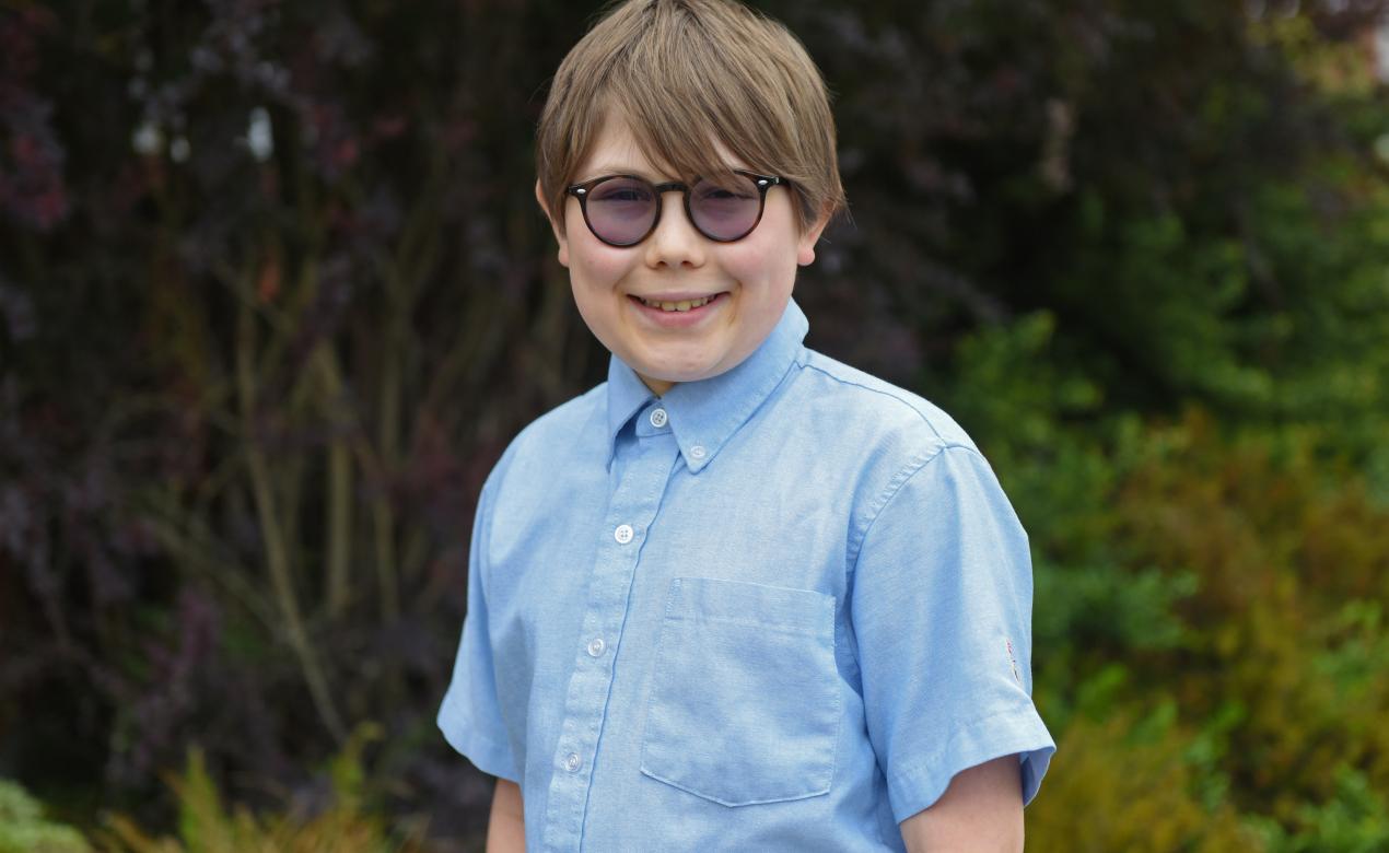 Middle School student Levi B. smiles for a photo in front of greenery