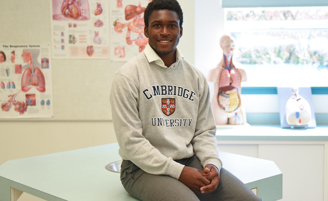Grade 12 student Dave Duru poses for a photo wearing a Cambridge University sweater while sitting in a biology lab