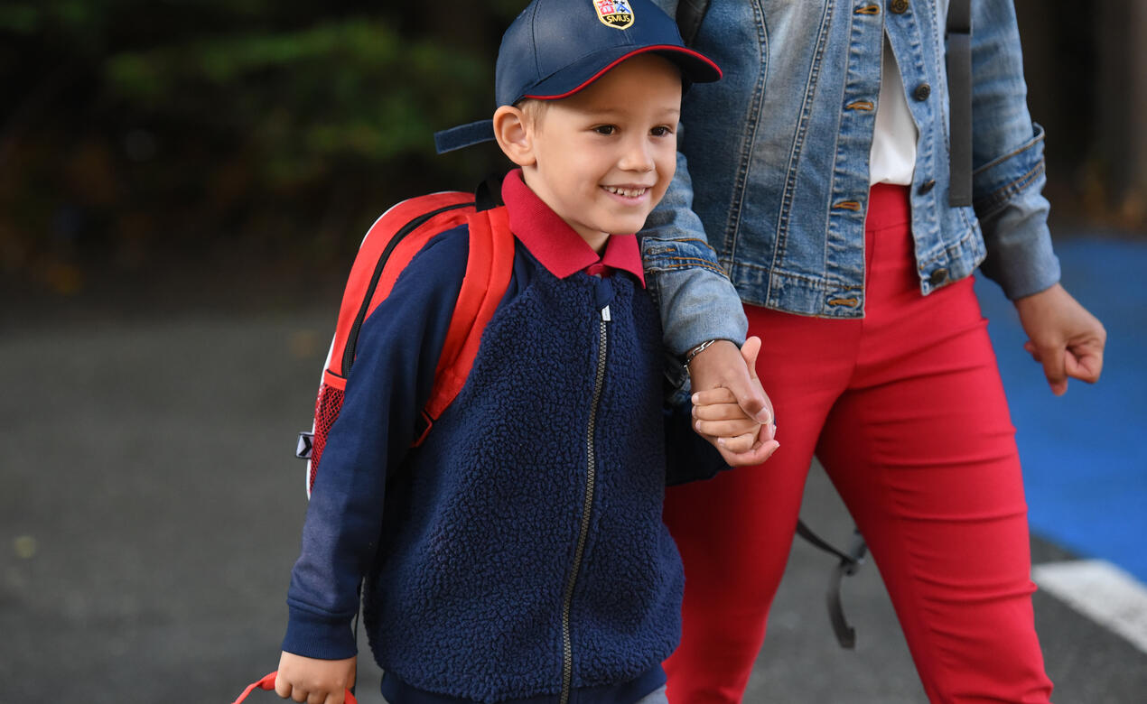 A Kindergarten smiles as they hold their parent's hand on the first day of school