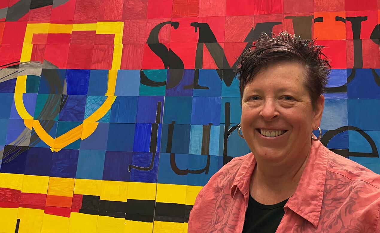A photo of Leanne Wilkins in front of a piece of Middle School artwork