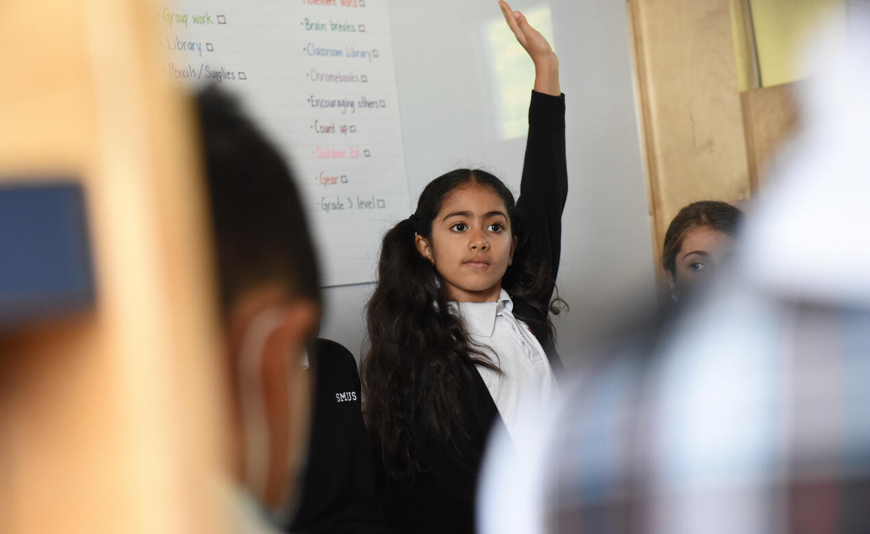 A Junior School student eagerly raises their hand in class