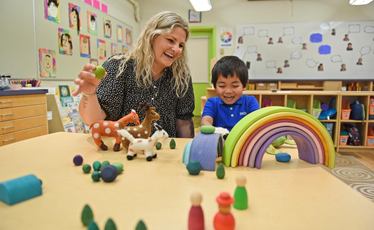 A teacher works alongside a happy Junior Kindergarten student