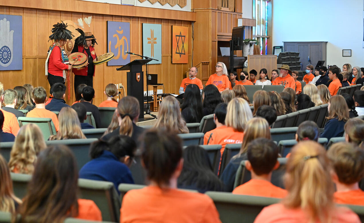 Students and teachers wearing orange shirts sit in the SMUS chapel listening to Bill White and Wes Edwards