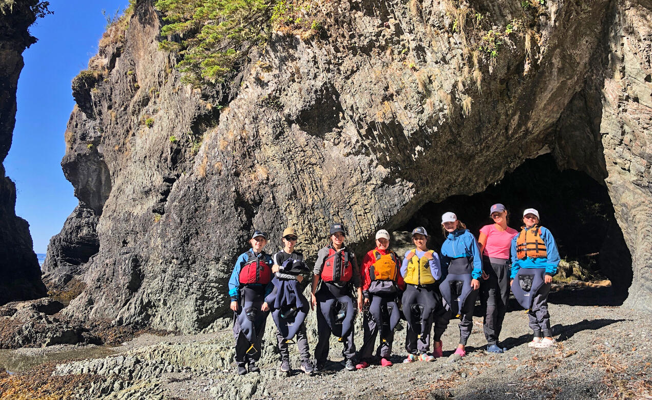 A group of students on an outdoor education trip pose in front of a beautiful rock