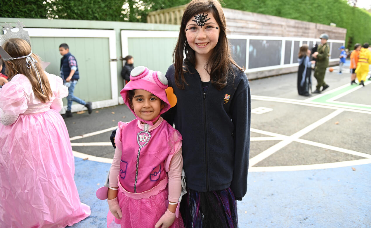 Two students wearing Halloween costumes smile together for a photo outside