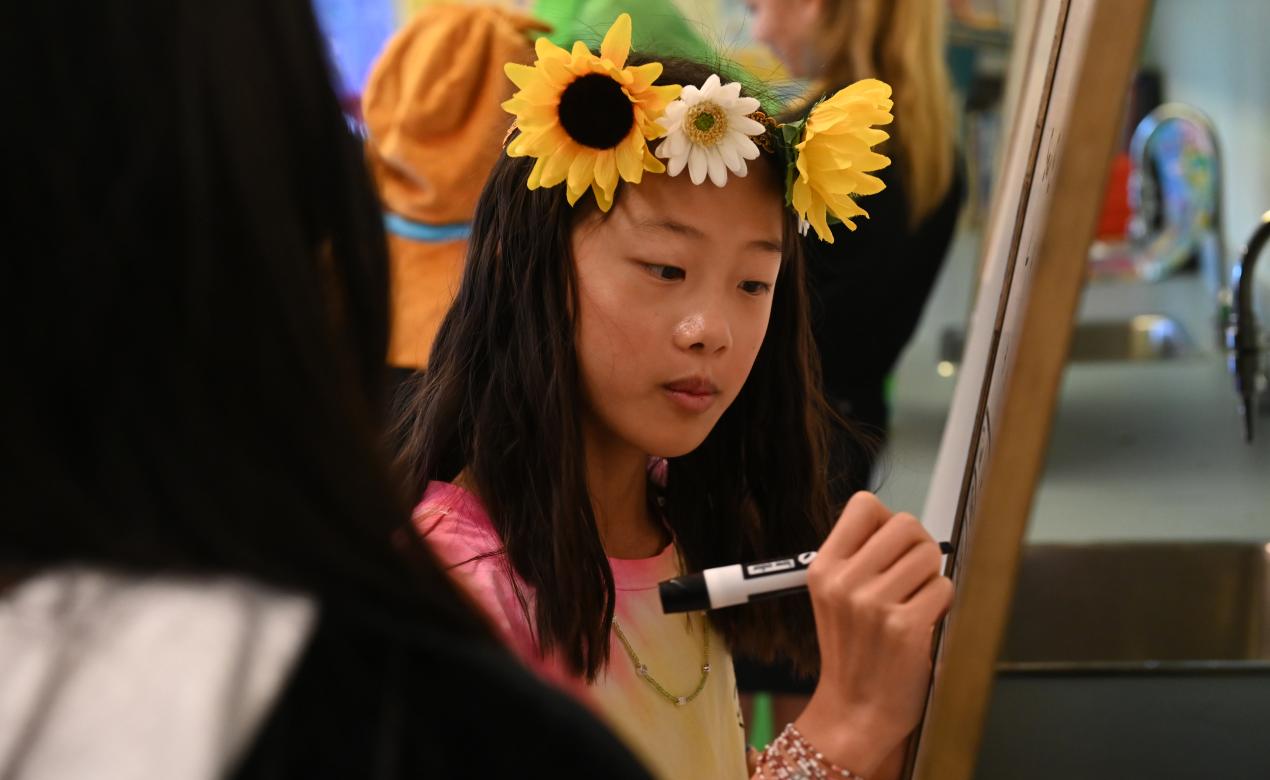 A student dressed as a hippie works at a whiteboard 