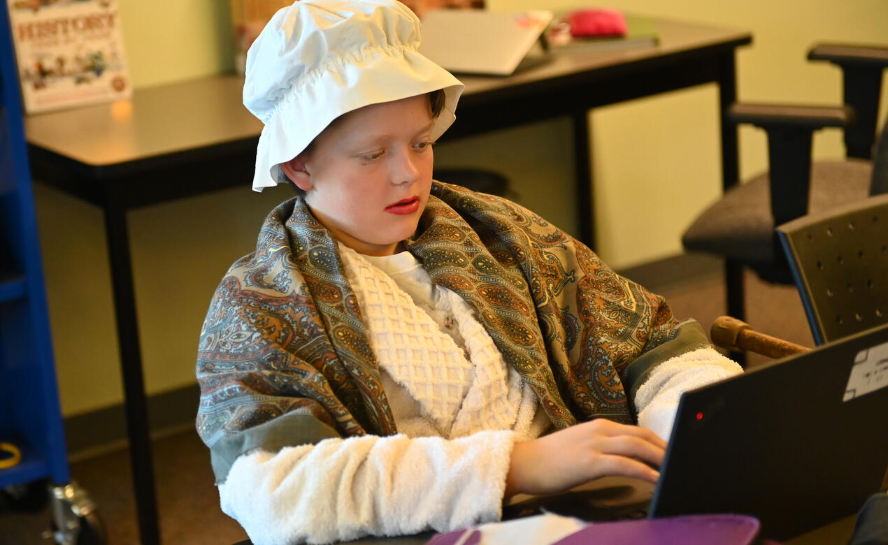 A Middle School student dressed as an old lady works on a laptop
