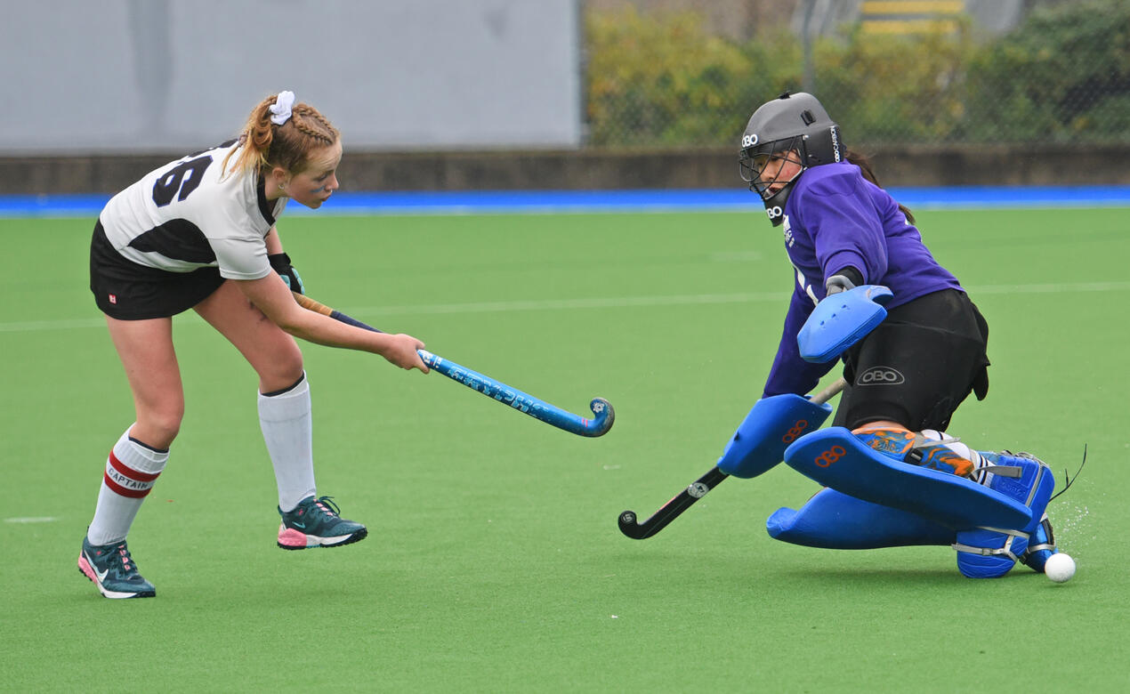 A Senior Girls Field Hockey player shoots the ball past an opposing goalie