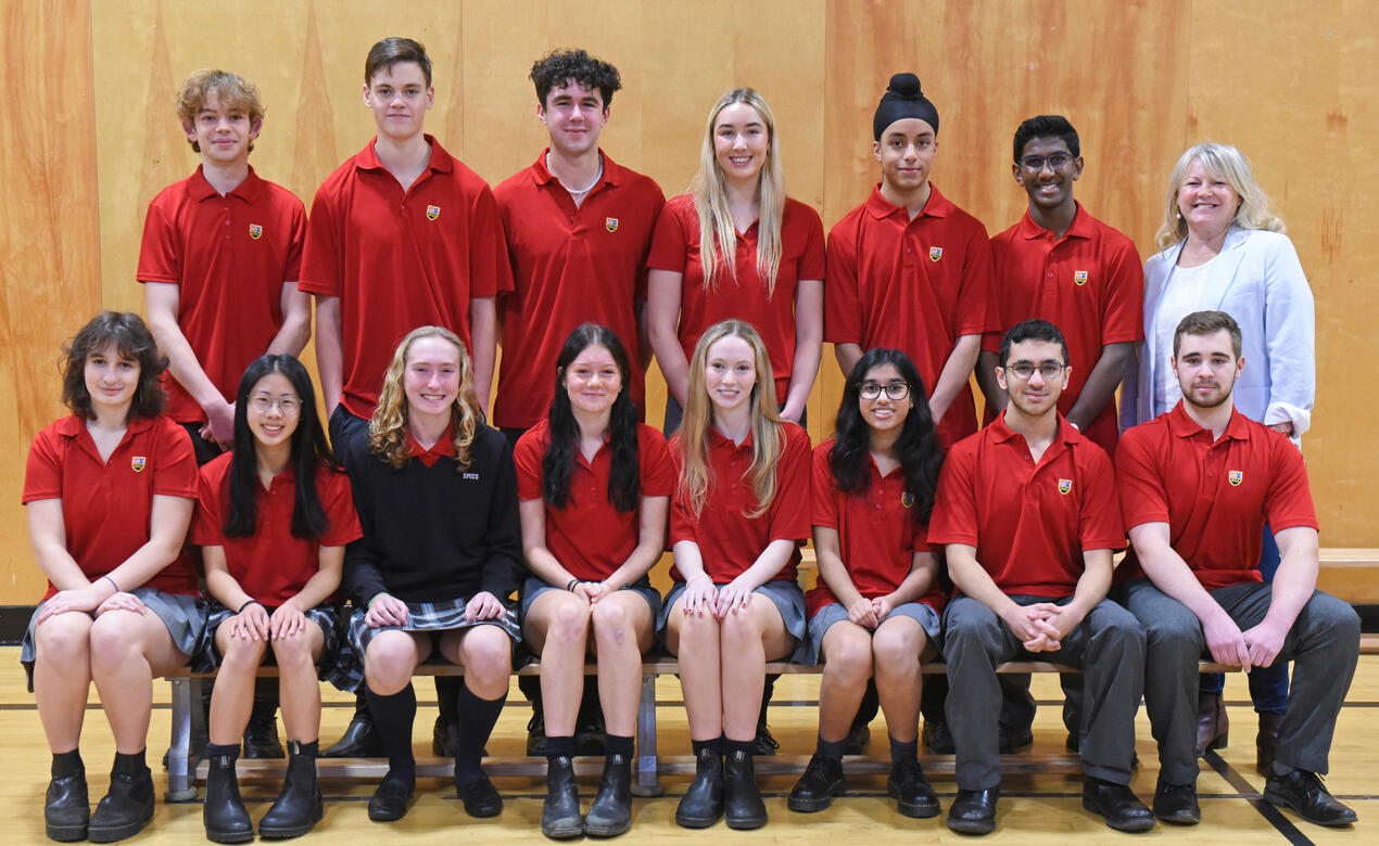 The Grade 12 Lifers from the Class of 2023 pose in their red shirts alongside former Kindergarten teacher Ms. Lincoln