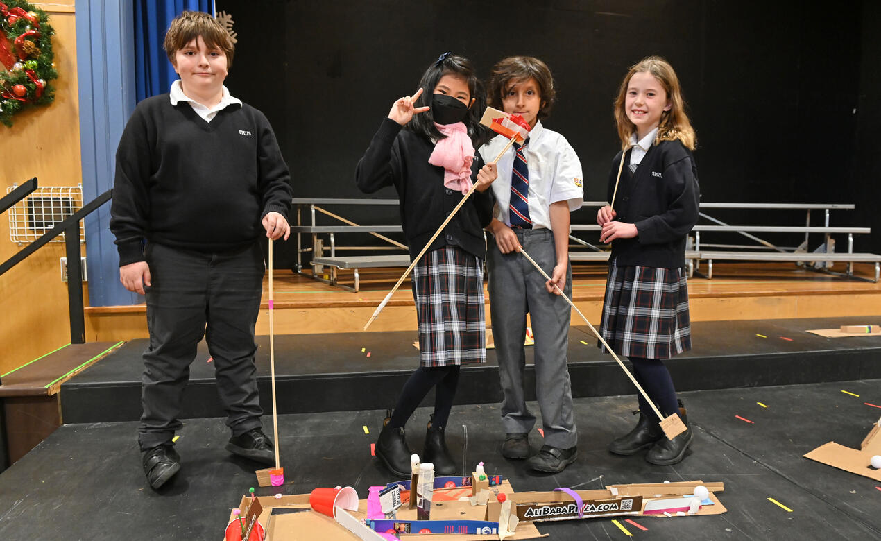 Four Grade 3 students pose with cardboard mini golf clubs and holes that they designed in Creators Club.