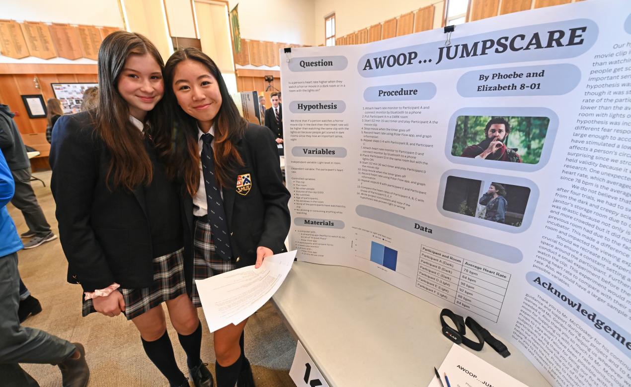 Middle School students Elizabeth and Phoebe smile for a photo beside their science fair project
