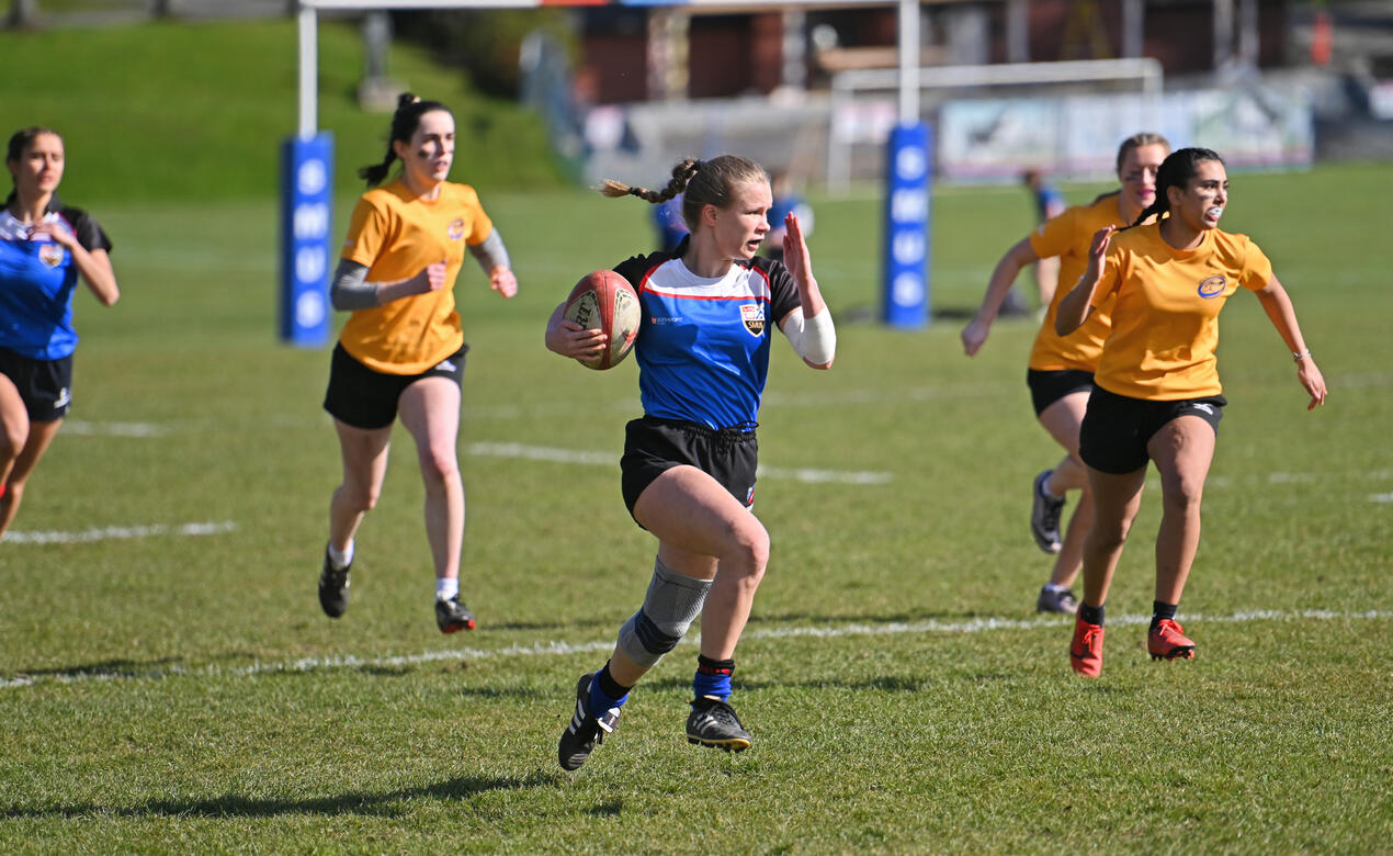 A Senior School Girls Rugby player runs down the field while being chased by opposing players
