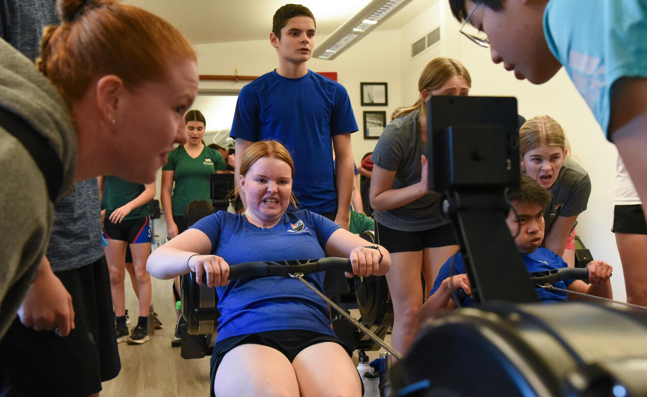 Egged on by teammates and coach, Juliet pushes herself on an erg