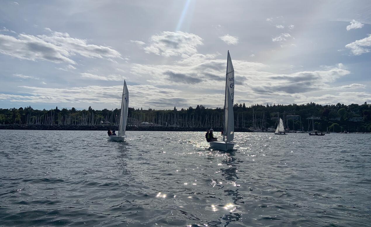 Two sailing boats out on open water with sun rays coming down