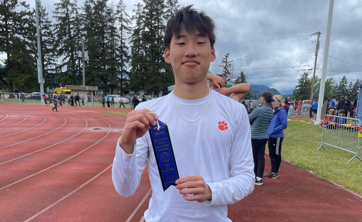 Leupold Wang stands at the side of the track holding a blue ribbon