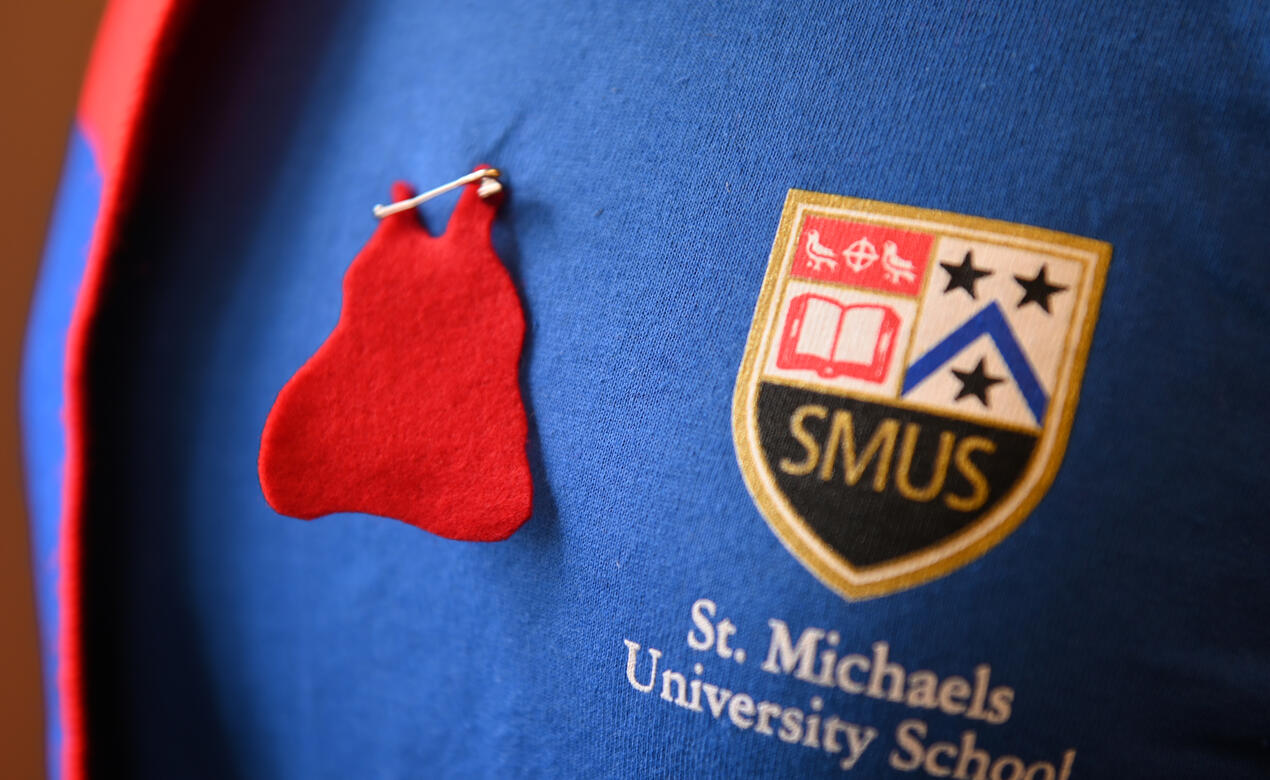 A red dress pin appears next to a SMUS logo on a t-shirt