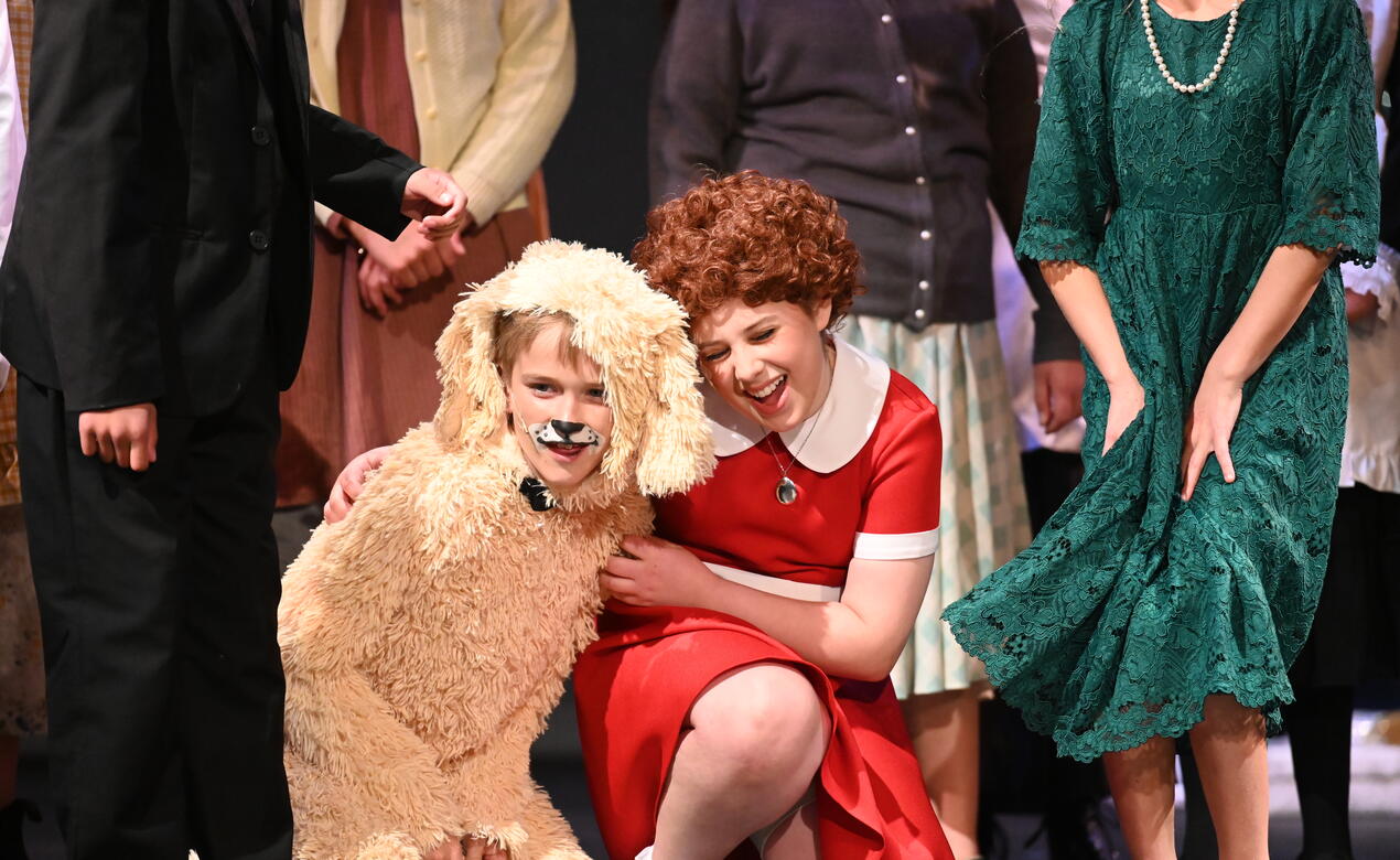 Grade 5 students acting as Annie and a dog embrace on stage at the Junior School musical.