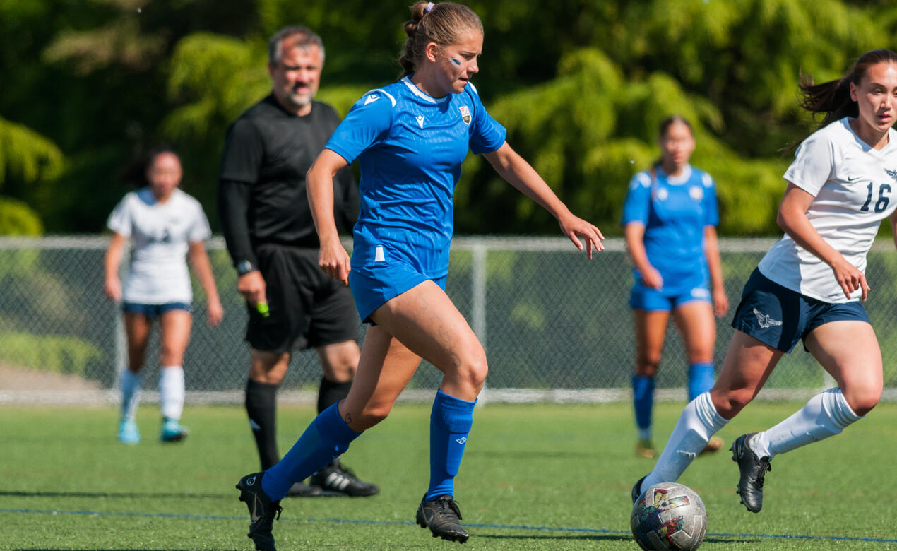 Senior girls soccer player dribbles up the field past an opponent