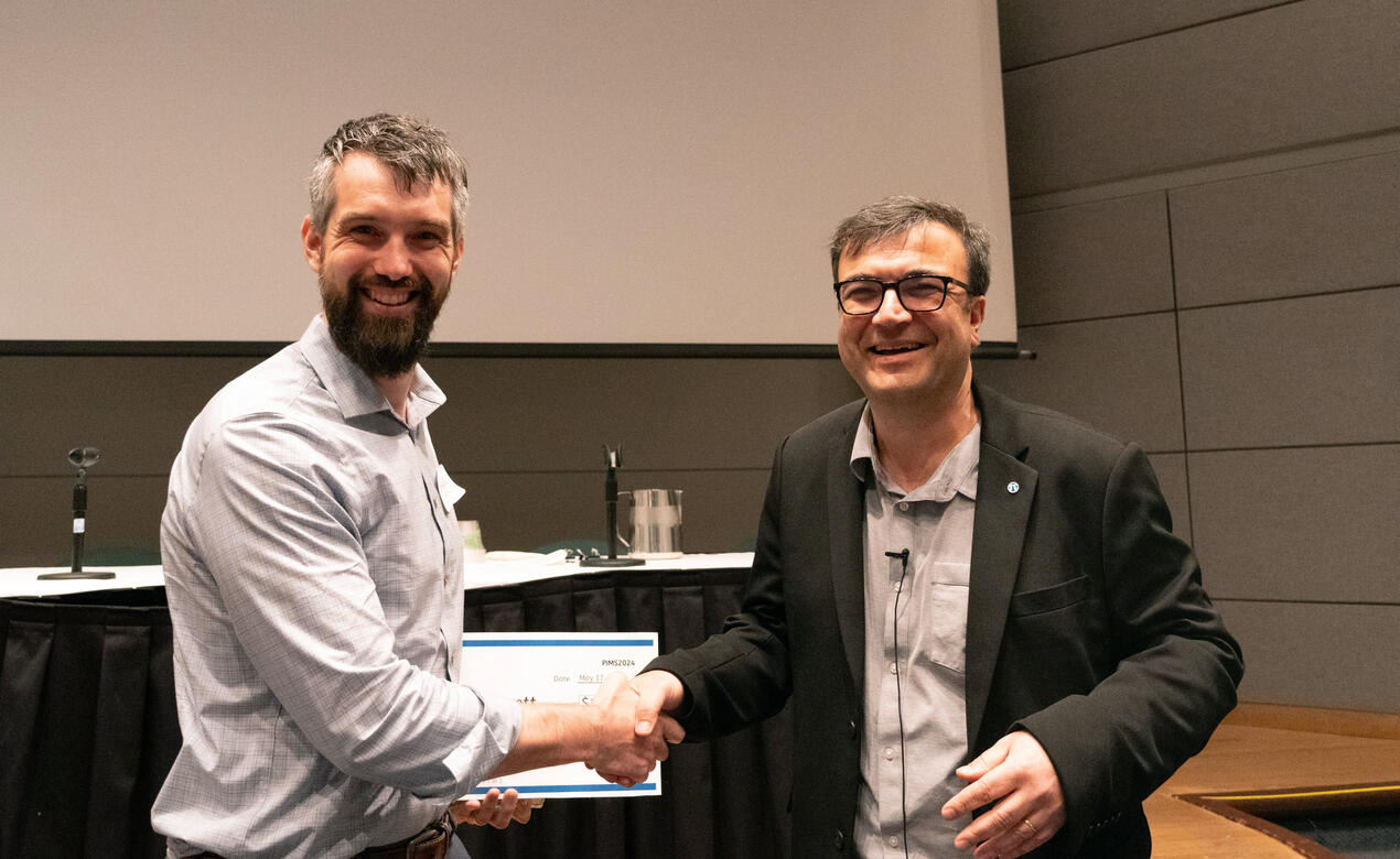 Alumni Trefor Bazett shakes hand with a presenter at the PIMS Conference as he receives his award certificate.