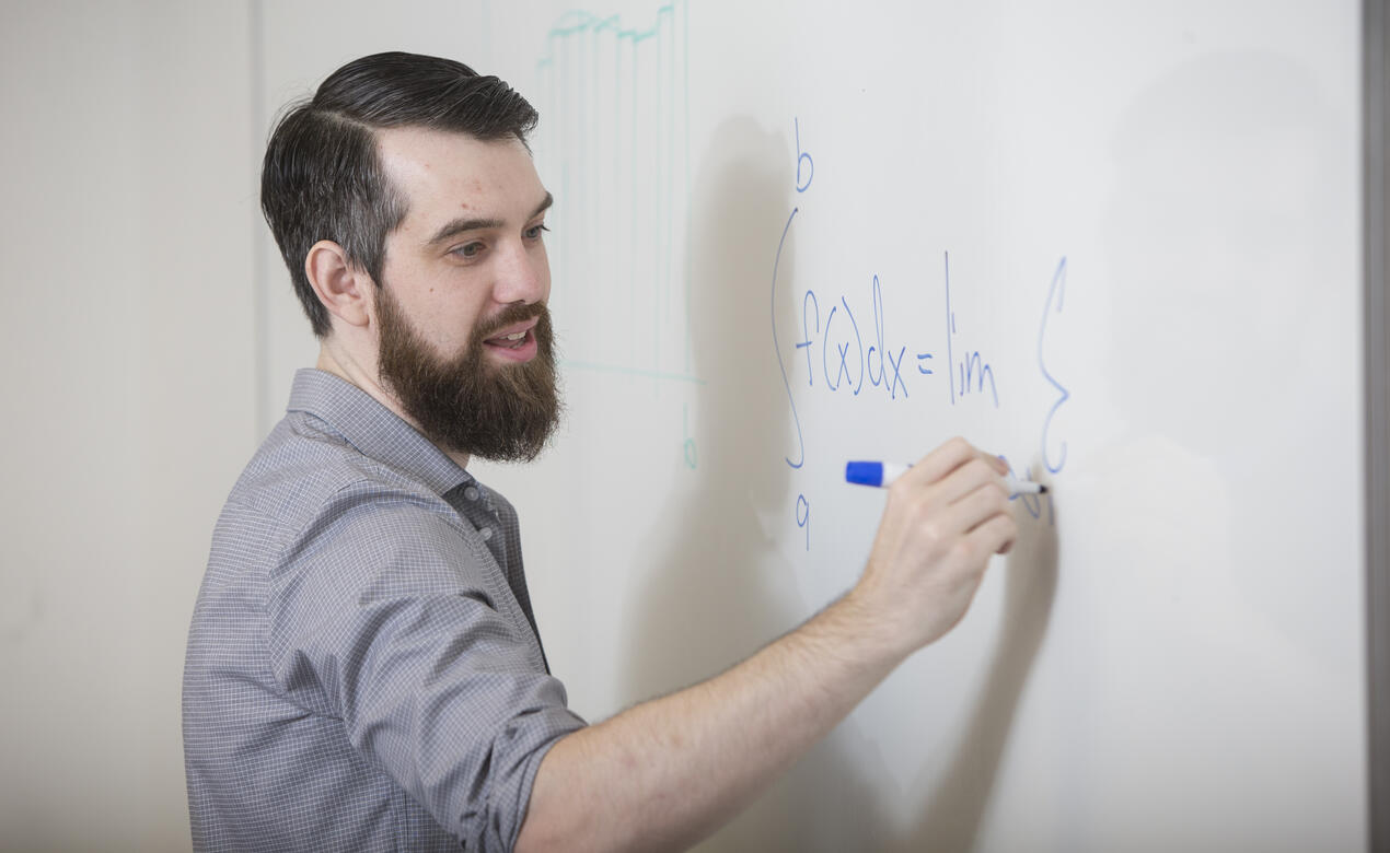 Alumni Dr. Trefor Bazett is writing a math equation on a white board while teaching a class.