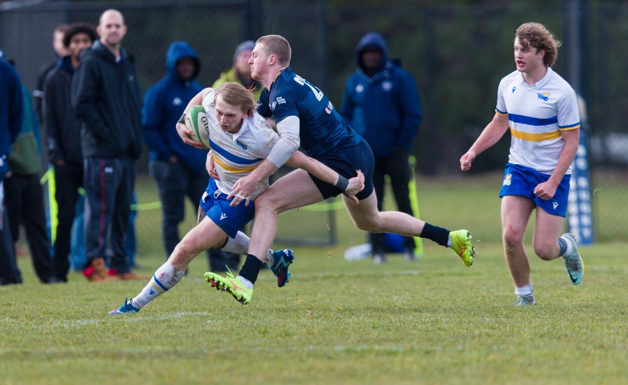 UVic rugby player Matthew Bennett keeps hold of a ball while being tackled in a rugby game