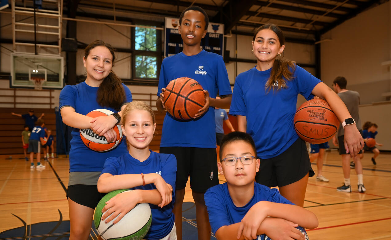 Group of five players taking a staged photo holding Basketballs
