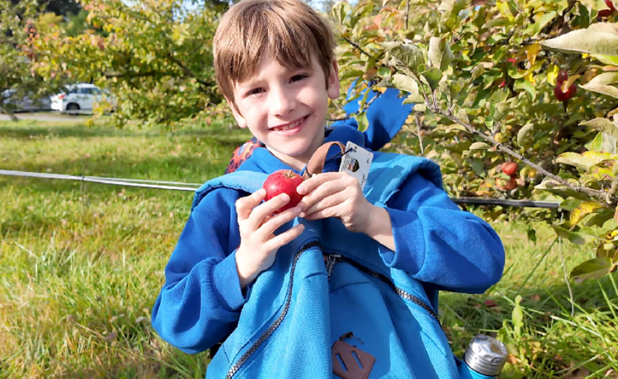 Grade 2 student holds up apple on Outdoor Ed trip to Sea Cider Farm