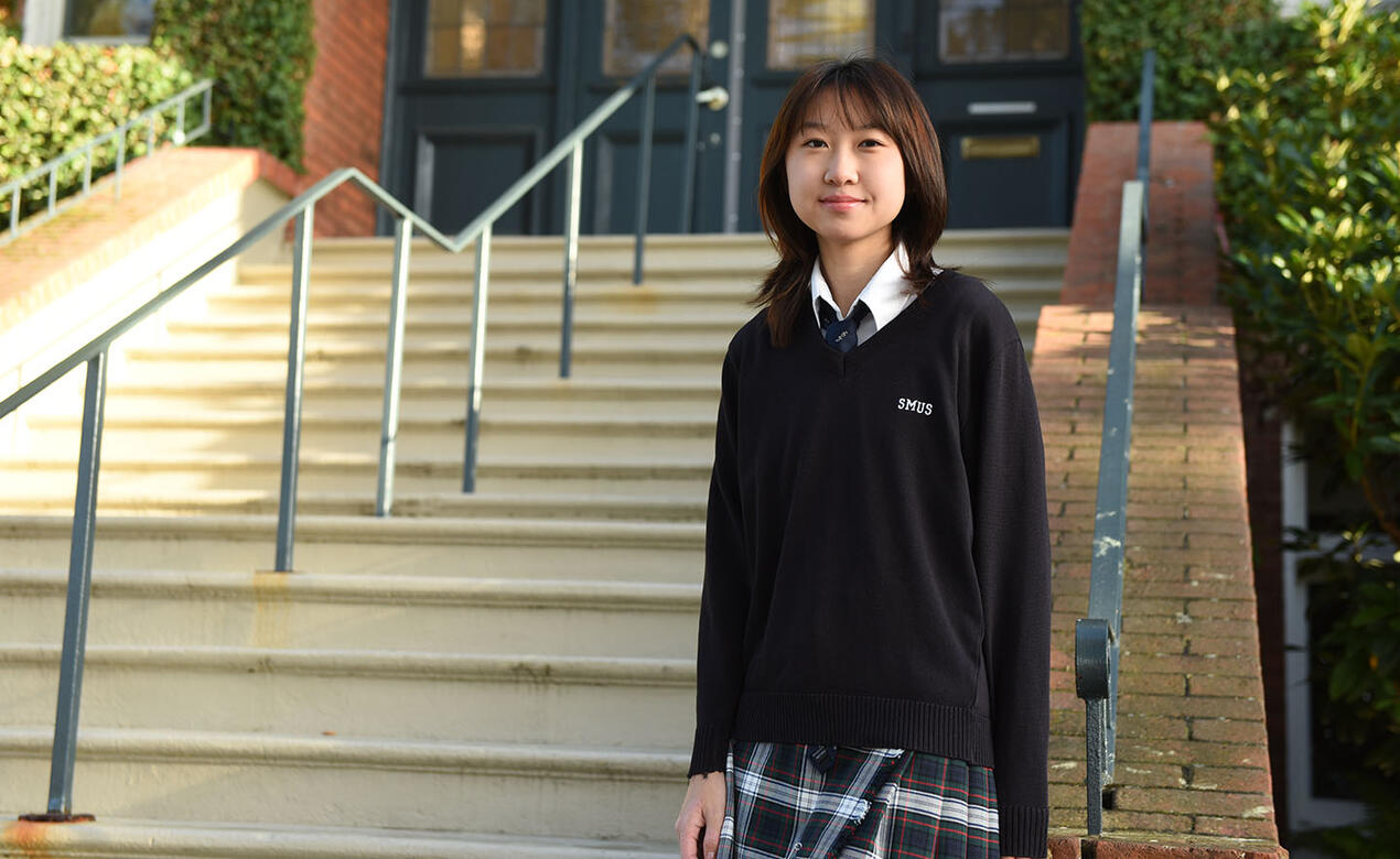 Senior School student Tina Wang '25 stands in front of steps at school house