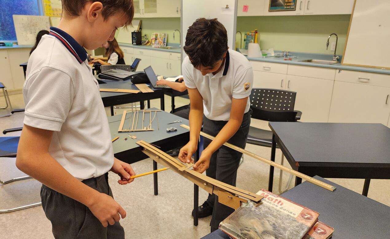 Two students glue cardboard and popsicle sticks together.