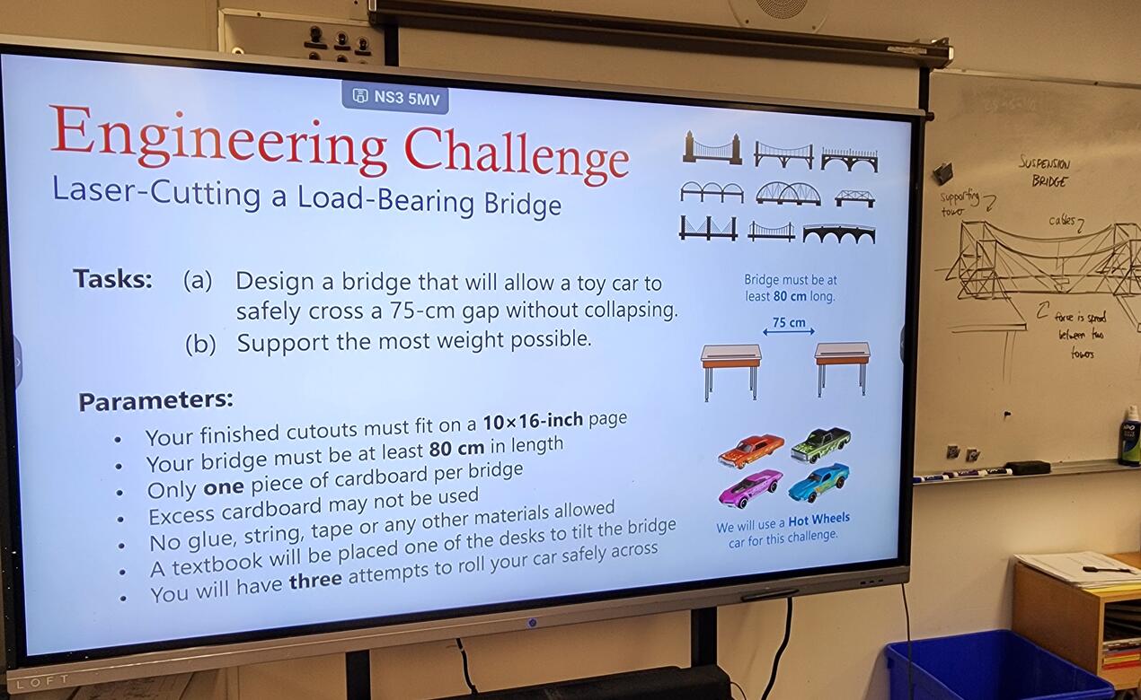 A TV screen projects the details of the Engineering Bridge Project challenge in a classroom.