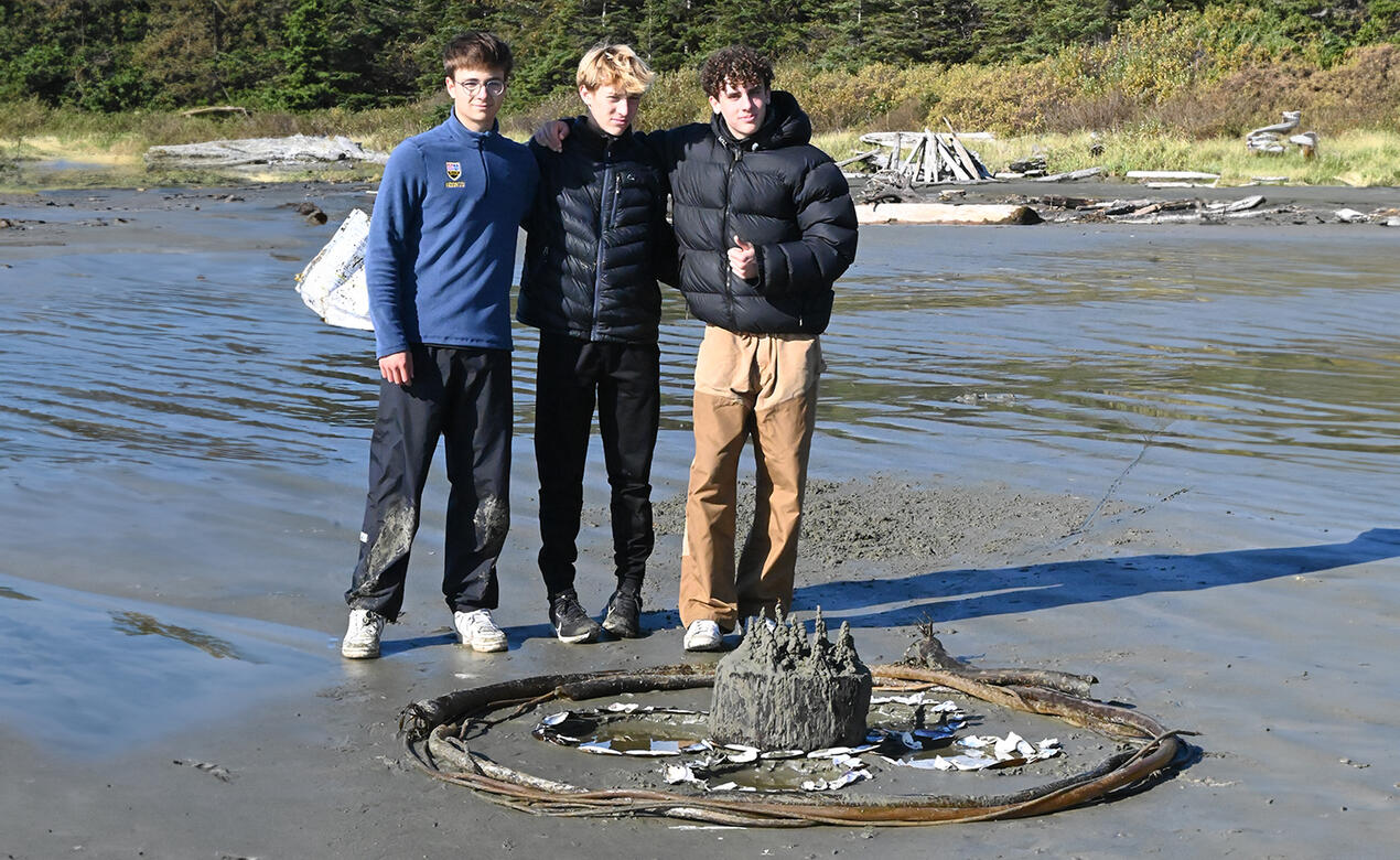 Grade 10 students stand with art on the beach in Tofino