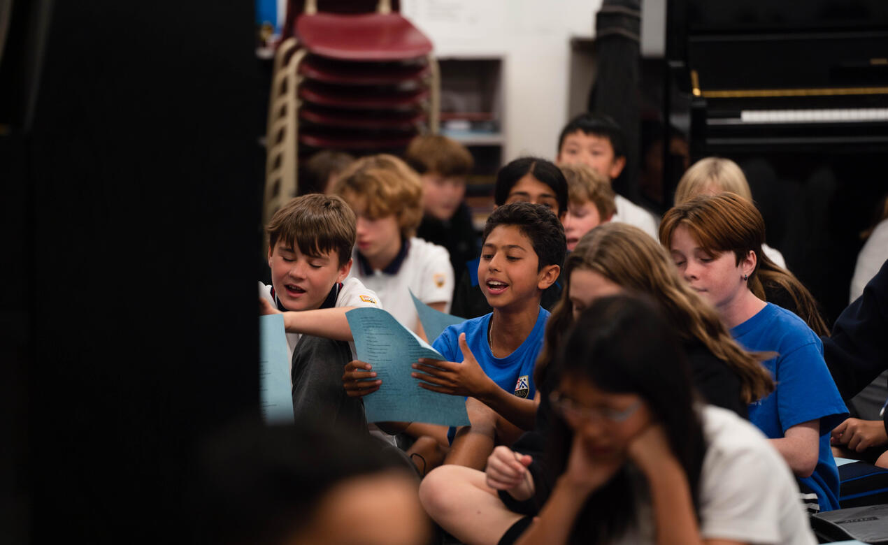 Middle School students are seated on the crowd singing during choir practice.