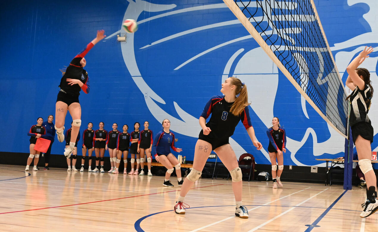 A SMUS player jumps high to spike the ball over the net