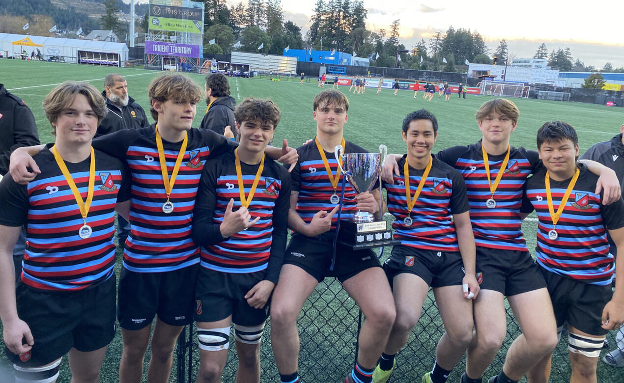 7 SMUS players wearing medals and holding a trophy stop for a group photo