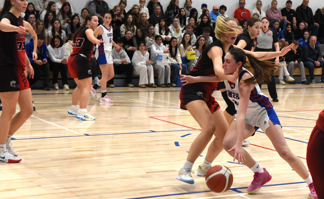 A SMUS basketball player collides with an opposing player in a rush to the basket