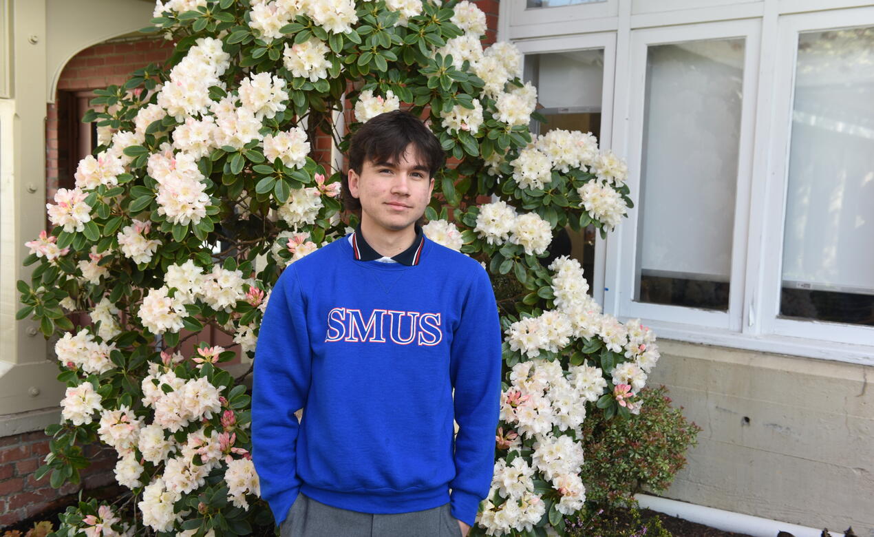 Alessandro Raniolo poses for a portrait photo in front of a beautiful bush of flowers on campus.