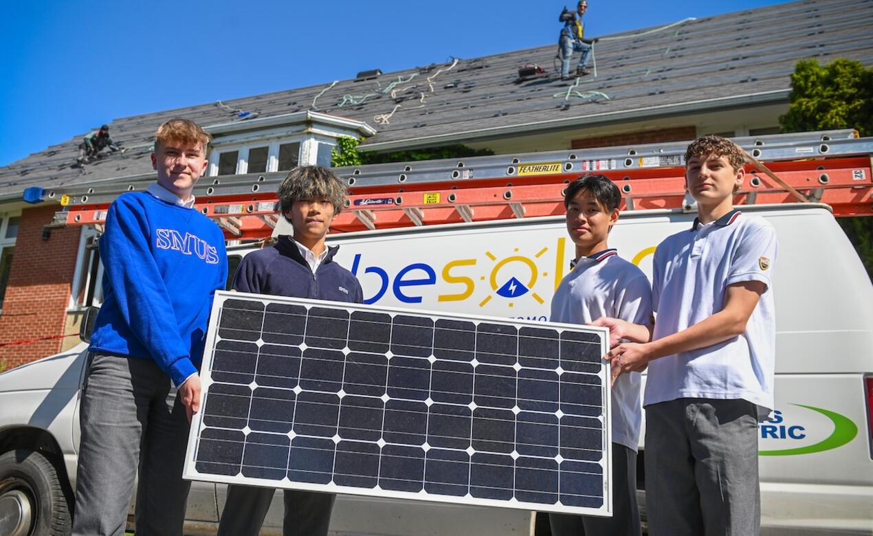 Four Econ 12 students hold up a solar panel that will be installed on the roof of brown hall.